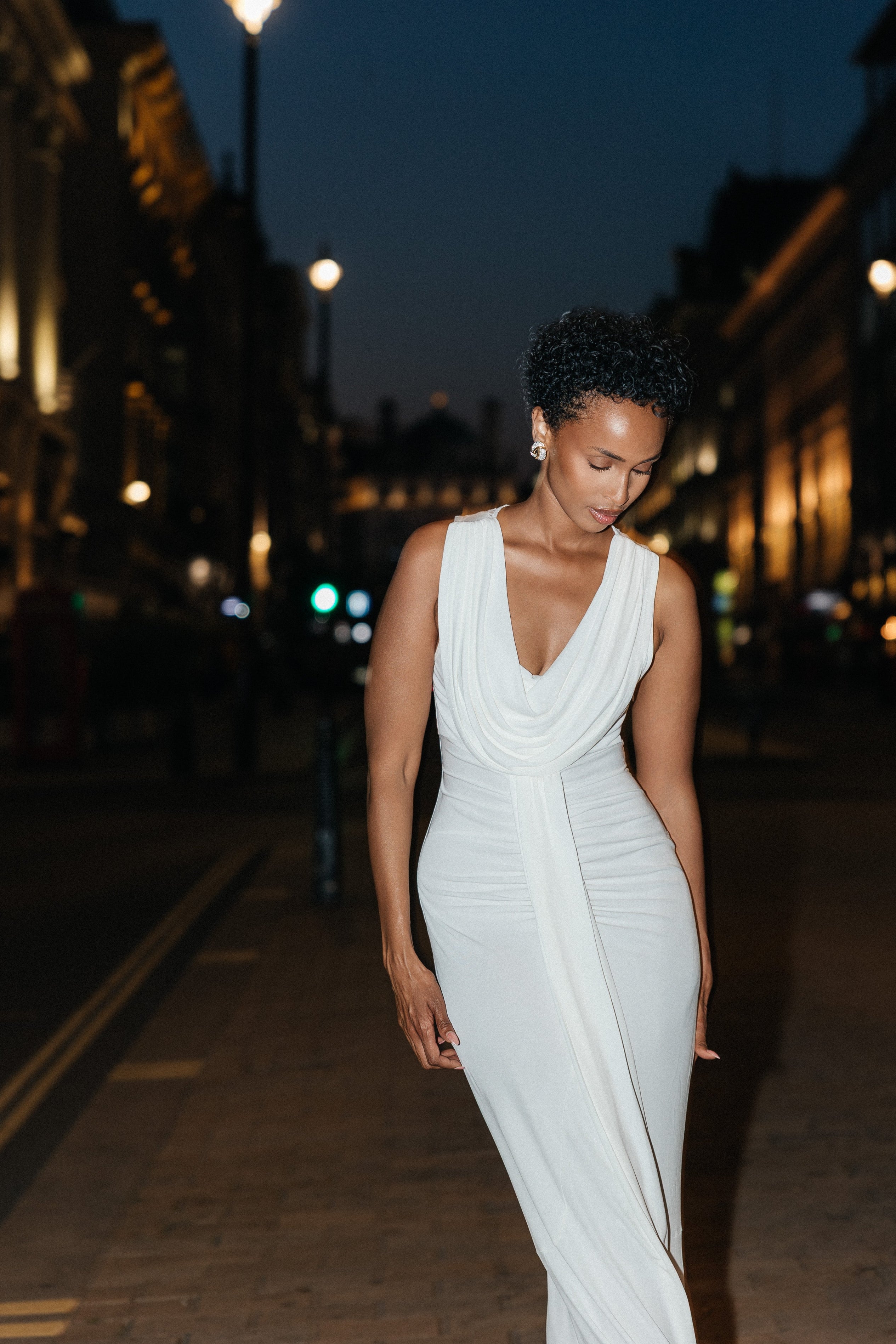 Woman in a white dress walking on a city street at night.